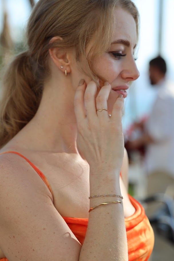 Woman wearing the Lucia Twist Cuff, a gold stainless steel twisted cuff bracelet layered with a permanent bracelet.