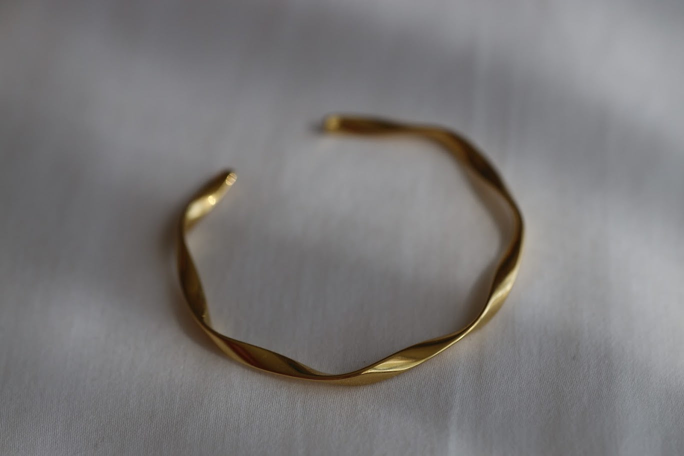 Gold stainless steel twisted open cuff bracelet with a polished finish on a white background.
