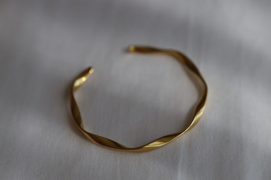 Gold stainless steel twisted open cuff bracelet with a polished finish on a white background.