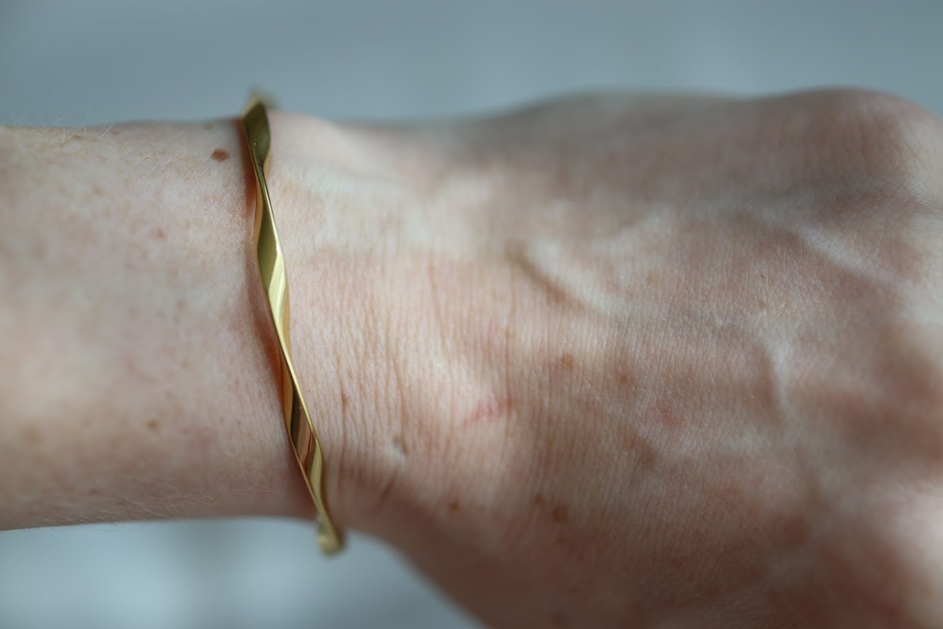 Close-up of the Lucia Twist Cuff, a gold twisted stainless steel cuff bracelet worn on the wrist.